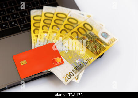 Banknotes of different denominations lie near the laptop, and from the top there is a plastic card Stock Photo