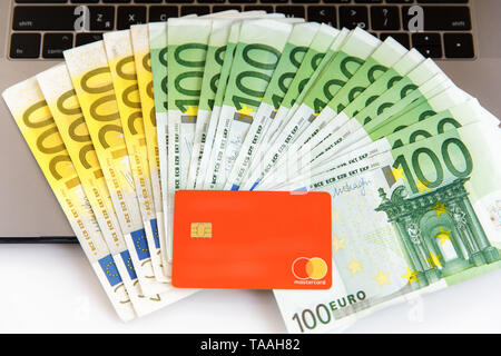 Banknotes of different denominations lie near the laptop, and from the top there is a plastic card Stock Photo