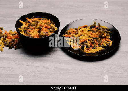 delicious colorful Italian pasta in two black ceramic plates on grey textured background, side view Stock Photo