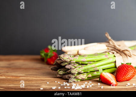 Fresh green and white asparagus with strawberries on rustic wooden table Stock Photo