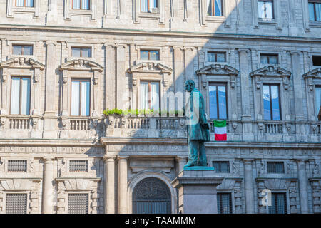 Milan, Italy - May 23 2019: People are wolking in the morning at square of San Fedele, statue of the writer Alessandro Manzoni with the Italian flag i