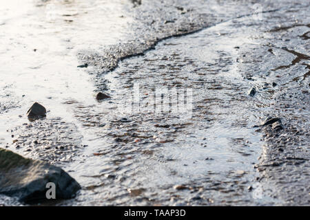 Ripples of murky water flowing along the beach on a grey, sad, moody day Stock Photo