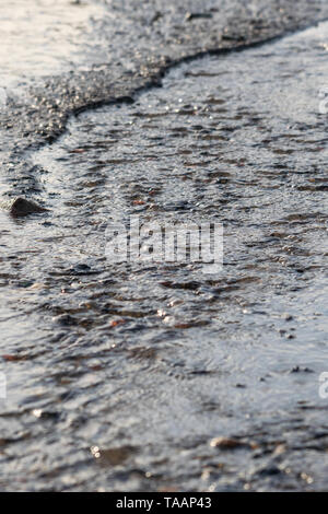 Ripples of murky water flowing along the beach on a grey, sad, moody day Stock Photo