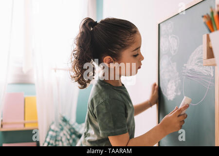 little girl drawing with a chalk on the chalkboard at her room at home, copy space for text Stock Photo