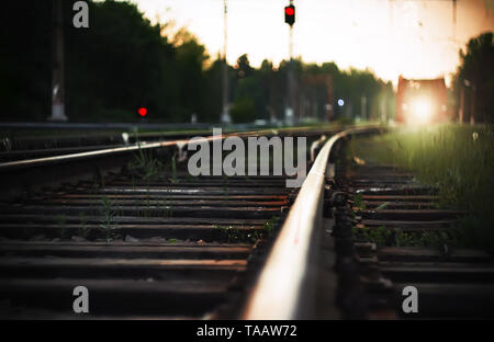 Bright light from the headlights of the approaching train, which rides on rails with wooden sleepers in the countryside. Next to the railway tracks ar Stock Photo