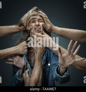 A young female model surrounded by male hands like her own thoughts or problems on dark background. Can't breathe and scream. Concept of mental deseas Stock Photo
