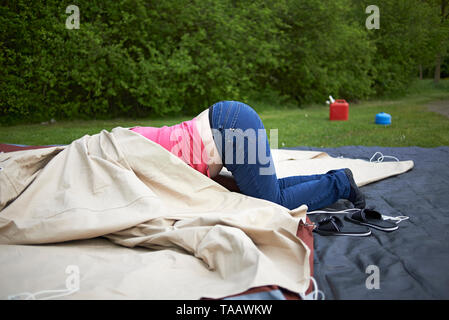 Funny image of a woman with her head inside a tent and her behind sticking out as she attempts to set up the tent outside on a camping ground