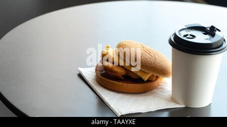 Bacon and Omelette Hamburger on the paper with White paper coffee mug on the table in fast food restaurant Stock Photo
