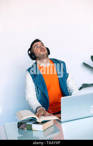Enjoying work and good music. Cheerful young man in headphones listening to the music while sitting at his working place Stock Photo