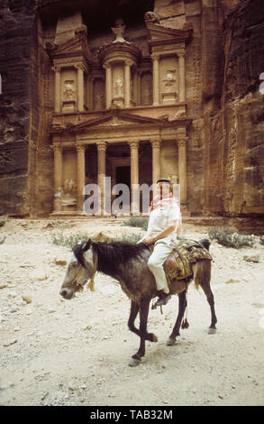 PETRA Jordan ancient city established 4th century BC as a trading hub to the trade route between Gulf of Arabic and Death sea.A man on donkey in front of old building built in the cliff Stock Photo