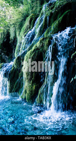 Beautiful Waterfall streaming down a fresh green hill into the turqouise water of the Lakes within the Plitvice National Park Stock Photo