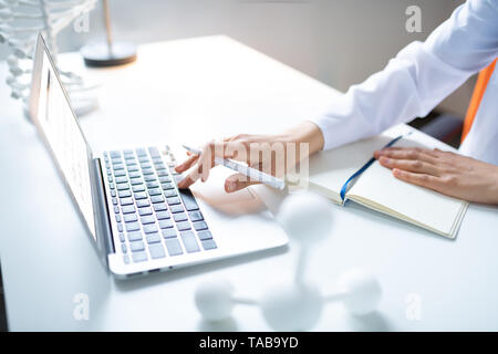 Typing on laptop. Close up of female scientist holding pen and typing something on laptop Stock Photo