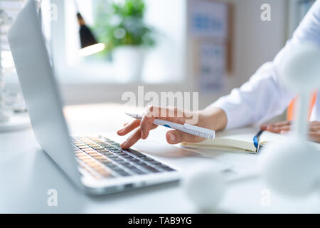 Holding white pen. Close up of female chemist holding white pen using laptop while searching information Stock Photo