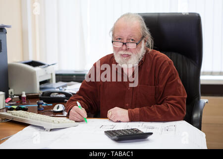 Architectural senior engineer working with blueprints and documents, writing on drawings. An architect bureau, one person Stock Photo