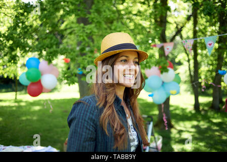 Happy close up of a Latina Brazilian woman wearing a straw hat outside in a park during a birthday celebration in spring sunshine Stock Photo