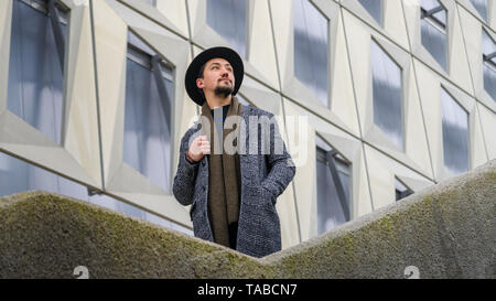 Portrait of a stylish handsome young man with a coat outdoors.  A man wearing a coat and a scarf looking away and wondering. Stock Photo