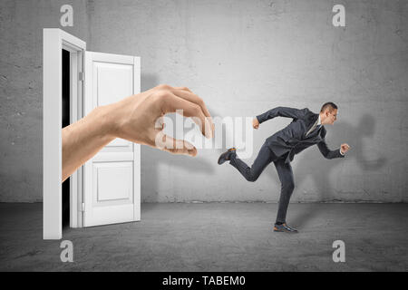 Side view of tiny businessman running from huge hand emerging from doorway behind. Stock Photo