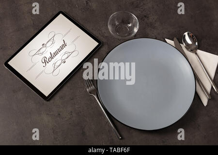 Tablet with stylish restaurant logo and laid table  Stock Photo
