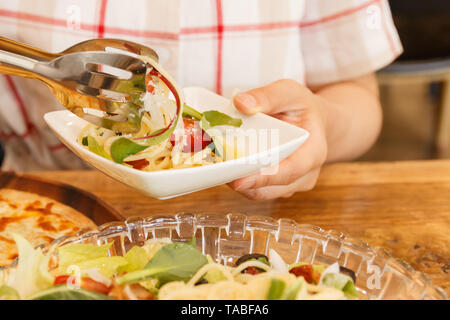 woman putting noodles into the dish on her hand Stock Photo
