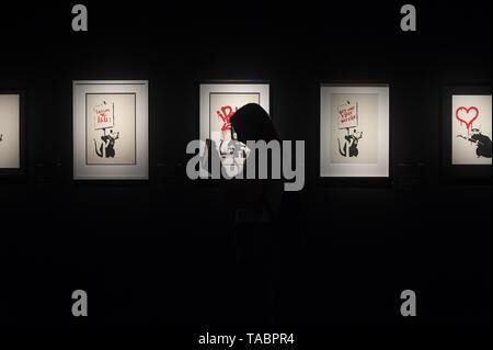 A visitor seen standing next to paintings during the exhibition. 'Banksy The art of Protest' at cultural center 'La Térmica' is an exhibition showing for the first time in Malaga. the work of famous and mysterious British street artist 'Banksy', display more than 40 creations such originals works, sculptures, videos and photographs provide by international private collections including the original print of 'Niña con globo'. Stock Photo