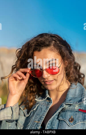 Portrait of young woman with curly brown hair wearing red sunglasses Stock Photo