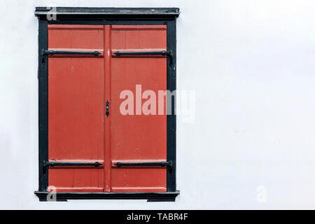 The rectangular window is covered with wooden shutters in red against the background of a wall of pale blue. From the window series of the world. Stock Photo