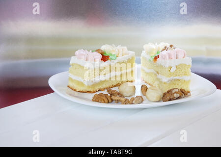 Sponge cakes soaked in brandy lie in a white plate next to scattered macadamia nuts and walnuts on a light background. Wooden table. Close-up. Dayligh Stock Photo