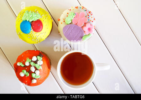 Delicious, multicolored cupcakes - Easter cakes and a cup of tea on a white wooden surface. Country breakfast. Homemade. Daylight. View from above Stock Photo