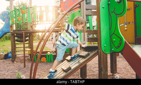 Photo of adorable toddler boy climbing and crawling on wooden staircase on children palyground at park Stock Photo