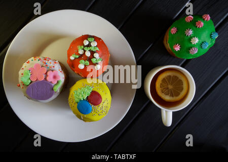 Multicolored cupcakes - Easter cakes in a white plate on a black background. Homemade. Daylight. View from above Stock Photo