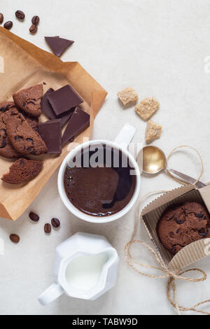 Oatmeal cookies with cocoa and chocolate on a brown craft paper and in a cardboard box, a cup of coffee and a milk jug Stock Photo