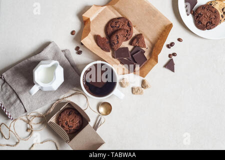 Oatmeal cookies with cocoa and chocolate on a brown craft paper and in a cardboard box, a cup of coffee and a milk jug Stock Photo