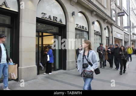 Shopping scene - young lady glancing at Zara store window while passing the store windows. Stock Photo