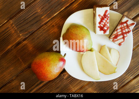 Homemade cakes and slices of red pear lie in a white plate on a wooden table made of pine boards. Buffet in authentic natural hotel. Summer still life Stock Photo