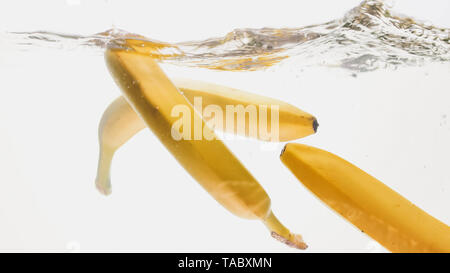 Closeup beautiful image of bananas falling in clear water against white background, Lots of air flaoting air bubbles and water splashes Stock Photo