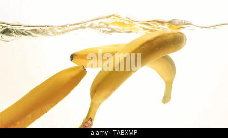 Closeup photo of fresh ripe yellow bananas falling and splashing in clear water against isolated white backgorund Stock Photo