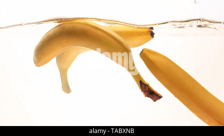 Closeup photo of fresh ripes fruits falling in water. Yellow sweet babanas splashing and flowing in water against white background Stock Photo