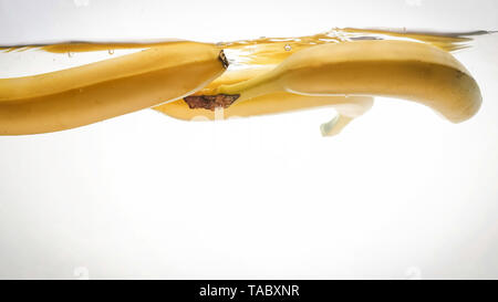 Closeup photo of fresh ripe yellow bananas falling and splashing in clear water against isolated white backgorund Stock Photo