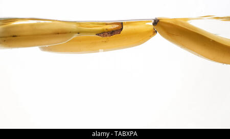 Closeup photo of fresh ripe yellow bananas falling and splashing in clear water against isolated white backgorund Stock Photo