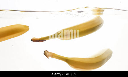 Closeup photo of fresh ripe yellow bananas falling and splashing in clear water against isolated white backgorund Stock Photo