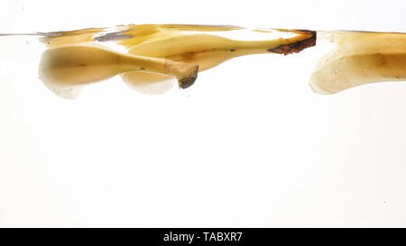 Closeup photo of fresh ripes fruits falling in water. Yellow sweet babanas splashing and flowing in water against white background Stock Photo