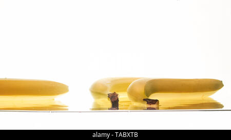 Closeup photo of fresh ripe yellow bananas falling and splashing in clear water against isolated white backgorund Stock Photo