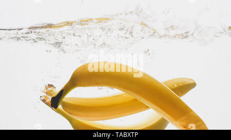 Closeup photo of fresh ripe yellow bananas falling and splashing in clear water against isolated white backgorund Stock Photo