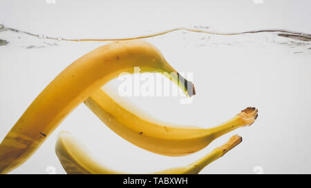 Closeup photo of fresh ripe yellow bananas falling and splashing in clear water against isolated white backgorund Stock Photo