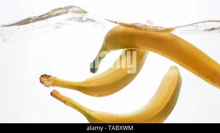 Closeup photo of fresh ripes fruits falling in water. Yellow sweet babanas splashing and flowing in water against white background Stock Photo