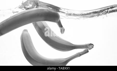 Closeup black and white image of fresh ripe banas falling and splashing. Tasty fruits floating in water Stock Photo