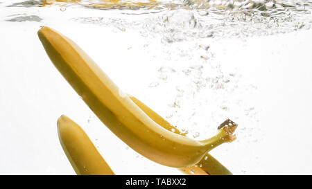 Closeup photo of fresh ripe yellow bananas falling and splashing in clear water against isolated white backgorund Stock Photo