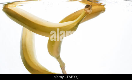 Closeup photo of fresh ripe yellow bananas falling and splashing in clear water against isolated white backgorund Stock Photo