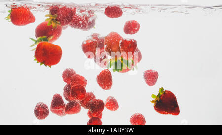 Closeup image of mixed berries falling and spalshing in water. Lots of raspberries and strawberries floating in water against white background Stock Photo