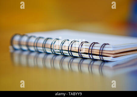 Spiral-bound notebook on a golden and blue background with reflection. Work in the office. Research and training. Shallow depth of field. Stock Photo